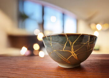 Zerbrochene Keramikschale, deren Risse mit goldener Farbe gefüllt sind. Symbol für Heilung und Würde trotz Bruchstellen.