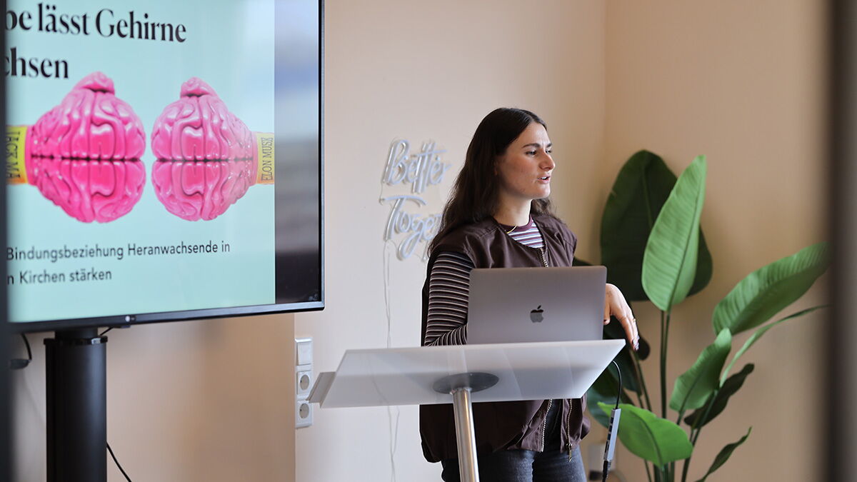 Eine Referentin steht an einem Rednerpult mit Laptop und präsentiert vor einer Leinwand mit Grafik zum Thema Gehirn und Entwicklung.