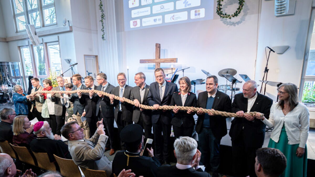 Vertreterinnen und Vertreter der VEF-MItgliedskirchen stehen vor einer Bühne und halten symoblisch ein dickes Tau gemeinsam in der Hand.