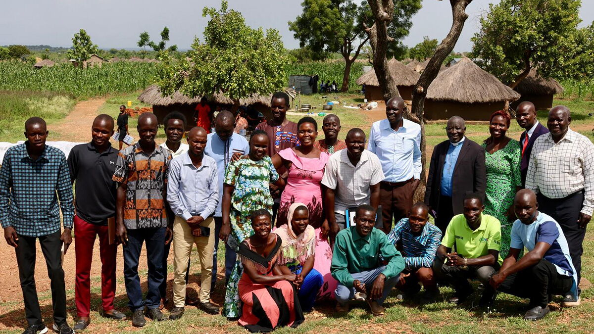 Lehrkräfte, Gemeindeleiterinnen und Gemeindeleiter sowie Studierende der Hope Bible School im Flüchtlingslager Rhino Camp in Norduganda vor traditionellen Rundhütten.