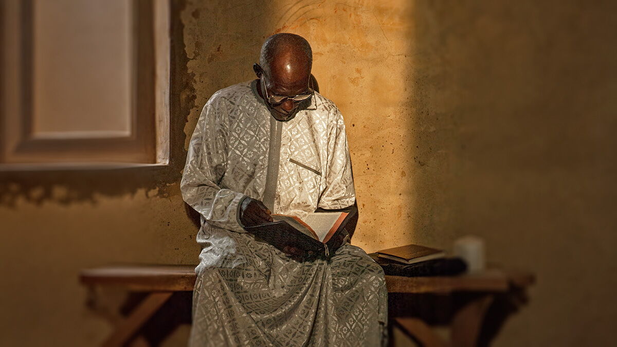 Ein älterer Mann sitzt in einer Kirche in Jos, Nigeria, und liest in einer aufgeschlagenen Bibel.