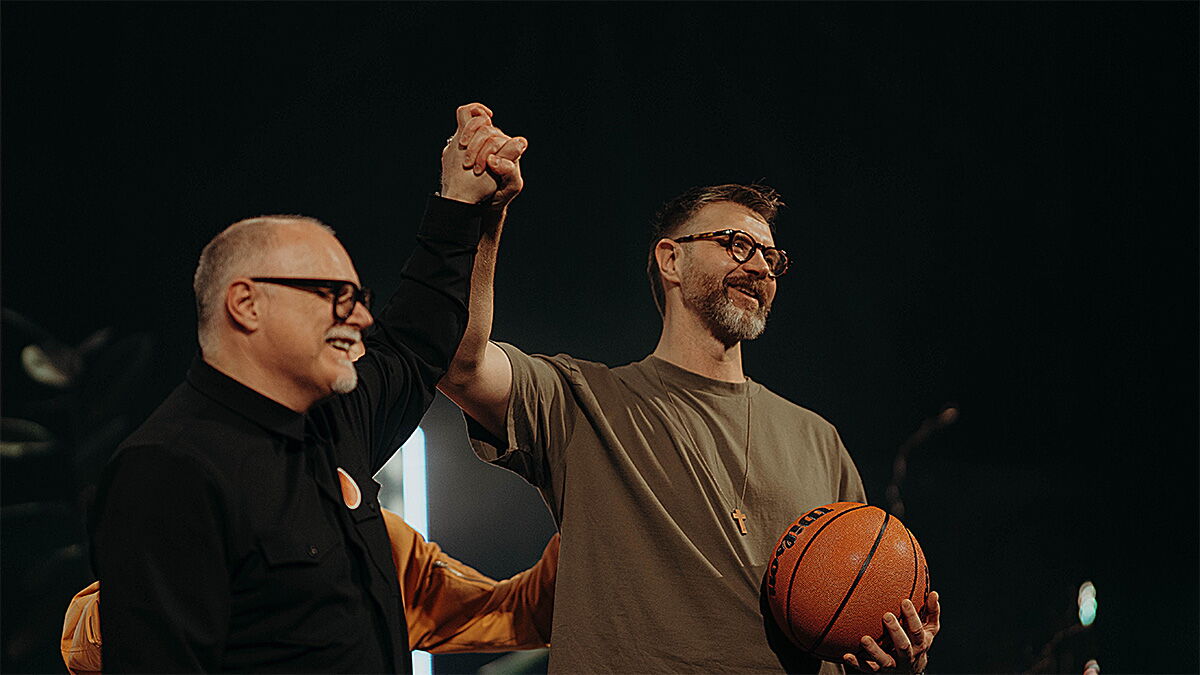 Zwei Männer, die gemeinsam die Hand hochhalten - der eine hat einen Basketball in der Hand.