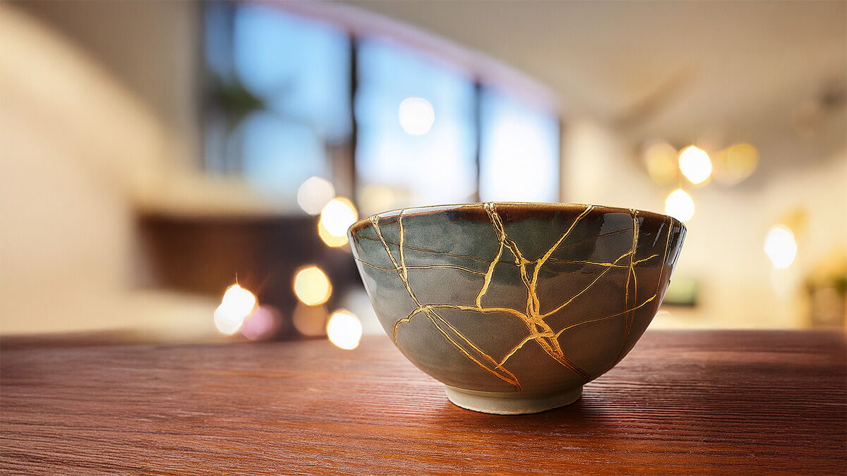 Zerbrochene Keramikschale, deren Risse mit goldener Farbe gefüllt sind. Symbol für Heilung und Würde trotz Bruchstellen.