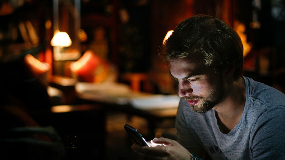 EIn junger Mann schaut konzentriert auf sein Smartphone.