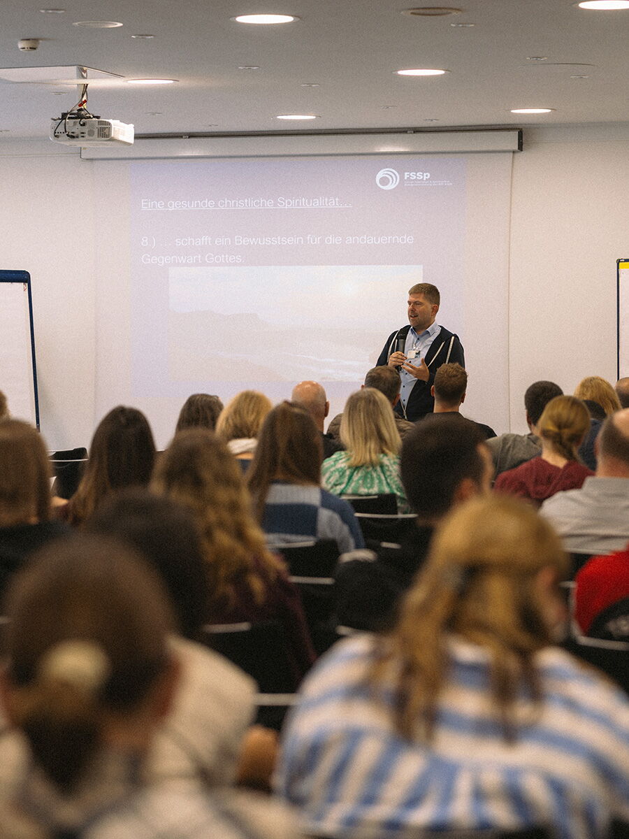 Pastor Nico Strobel spricht vor einem gut besetzten Konferenzraum über gesunde christliche Spiritualität. Hinter ihm ist eine Präsentationsfolie des FSSp zu sehen.