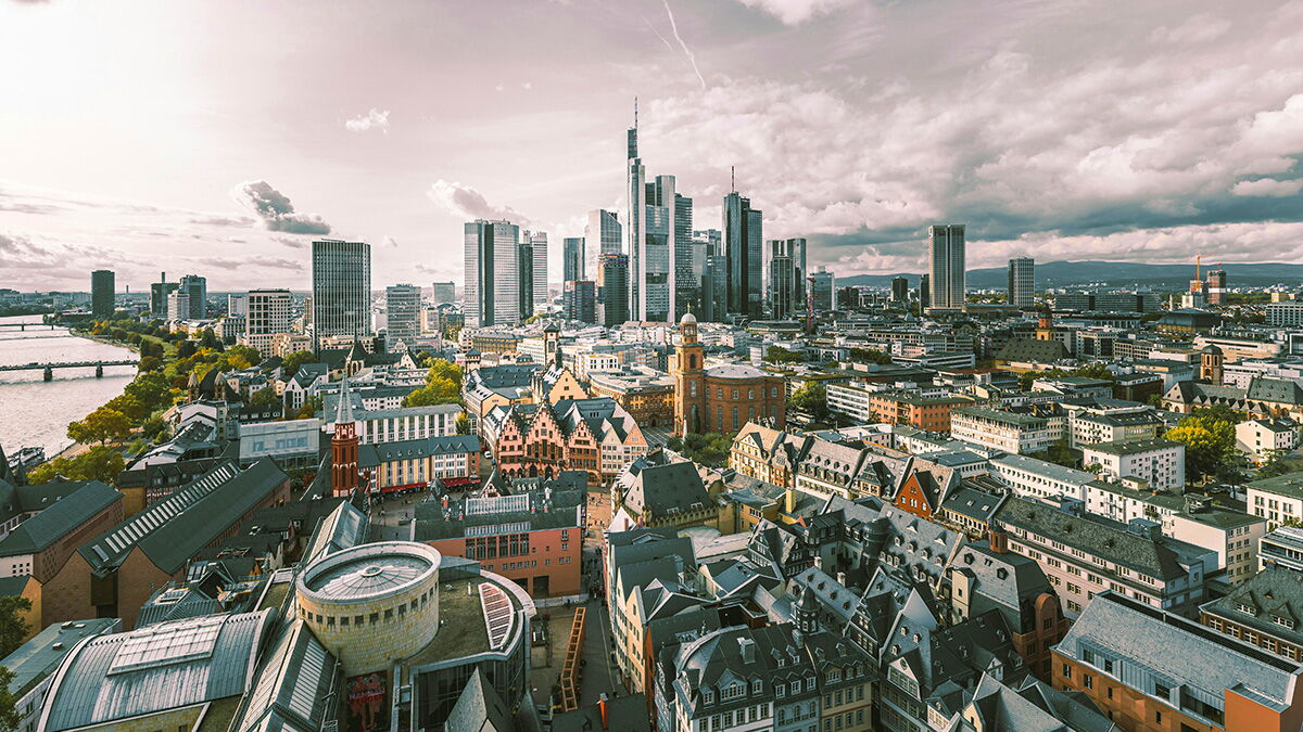 Panoramablick auf Frankfurt am Main mit Hochhäusern der Skyline im Hintergrund, historischen Gebäuden im Vordergrund und dem Fluss Main auf der linken Seite.
