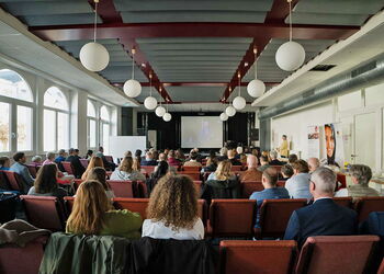 Großer Saal mit zahlreichen Teilnehmern, die einer Präsentation auf einer Bühne beim Forumstag in Erzhausen zuhören.