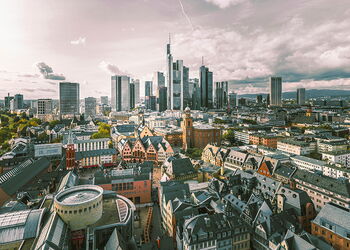 Panoramablick auf Frankfurt am Main mit Hochhäusern der Skyline im Hintergrund, historischen Gebäuden im Vordergrund und dem Fluss Main auf der linken Seite.