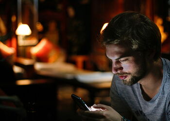 EIn junger Mann schaut konzentriert auf sein Smartphone.