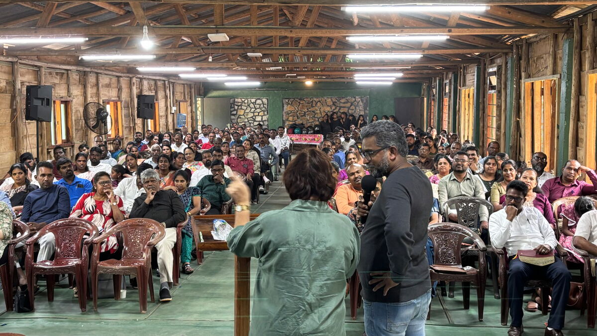 Zwei Menschen stehen auf einer Bühne mit dem Rücken zum Fotografen, davor Menschen, die zuhören.