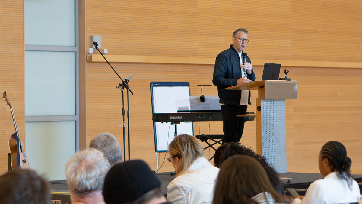 Ein Mann steht an einem Rednerpult und hält einen Vortrag vor einem Publikum in einem großen Konferenzsaal.