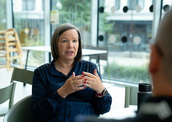 Eine Frau sitzt an einem Tisch im Gespräch mit einer anderen Person und erläutert mit Gesten ein Thema. Die Szene steht beispielhaft für Seelsorge, geistliche Begleitung und persönliche Beratung.