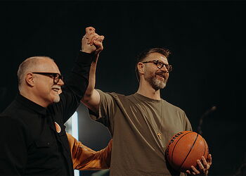 Zwei Männer, die gemeinsam die Hand hochhalten - der eine hat einen Basketball in der Hand.