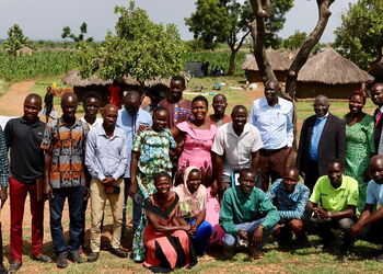 Lehrkräfte, Gemeindeleiterinnen und Gemeindeleiter sowie Studierende der Hope Bible School im Flüchtlingslager Rhino Camp in Norduganda vor traditionellen Rundhütten.