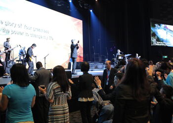 Bühne, Live-Band und Großbildleinwand; zahlreiche Teilnehmende stehen im Vordergrund, viele mit erhobenen Händen.
