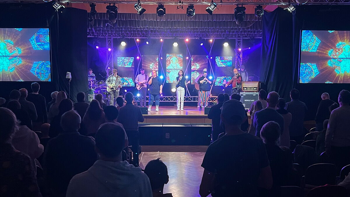 Eine Band spielt auf einer Bühne beim Lobpreis und die Teilnehmer stehen davor.
