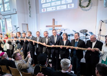 Vertreterinnen und Vertreter der VEF-MItgliedskirchen stehen vor einer Bühne und halten symoblisch ein dickes Tau gemeinsam in der Hand.