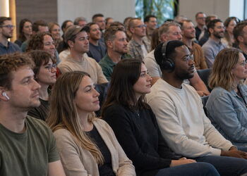 Eine Gruppe von Männern und Frauen sitzt in einem Gottesdienstraum und hört aufmerksam zu; einige tragen Kopfhörer, um eine Übersetzung der Predigt zu verfolgen.